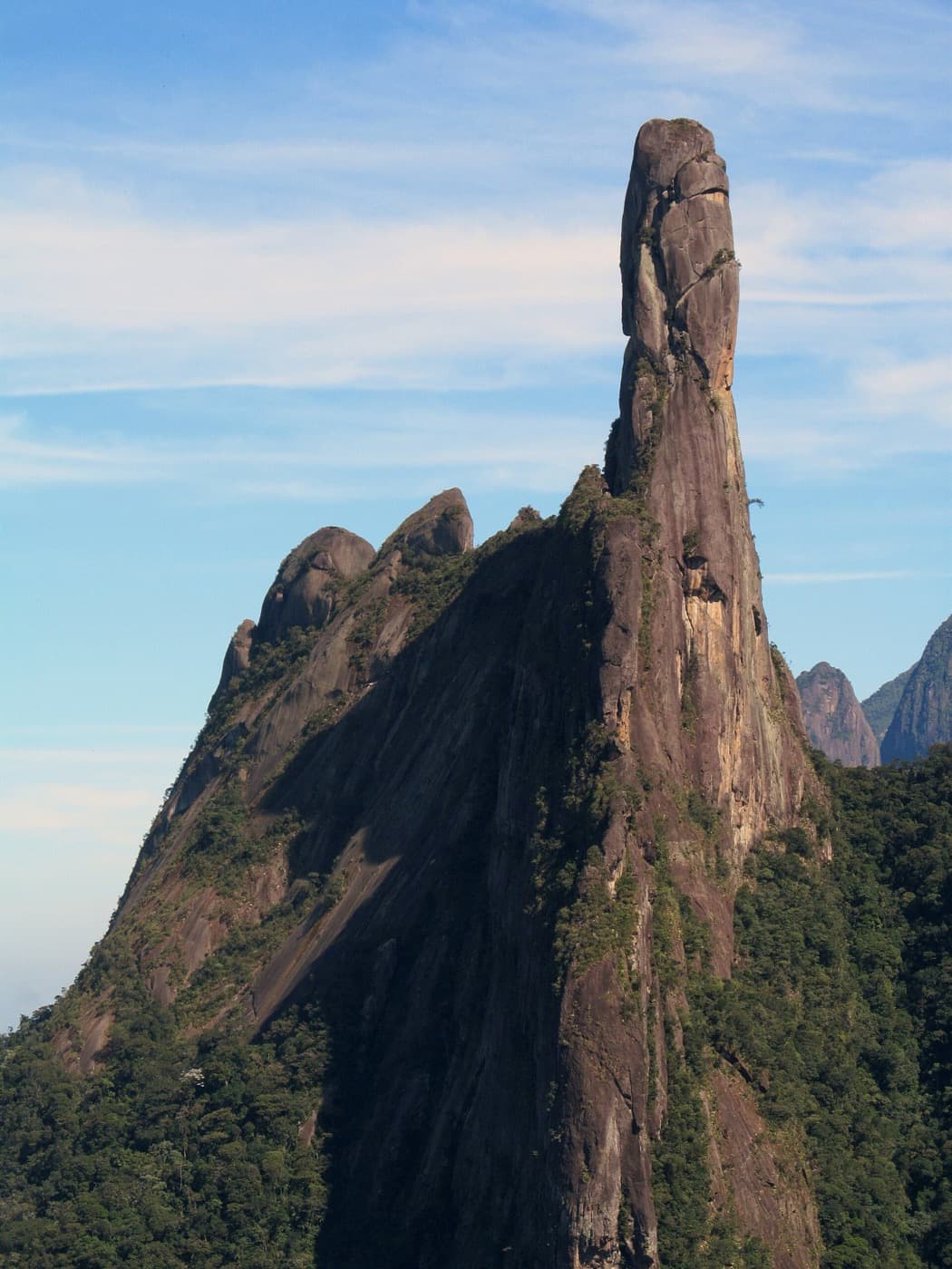 Torre final do Dedo de Deus vista de perto, com a parede de granito e a mata na base
