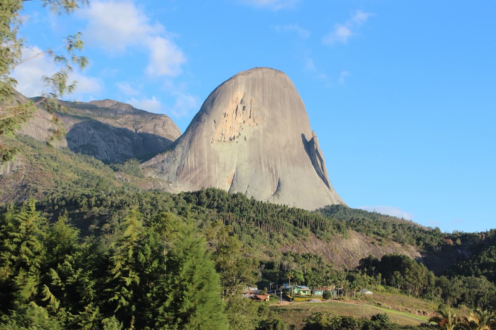 Pedra Azul em Domingos Martins sob céu azul, com a saliência da Pedra do Lagarto na face direita e mata no pé da rocha