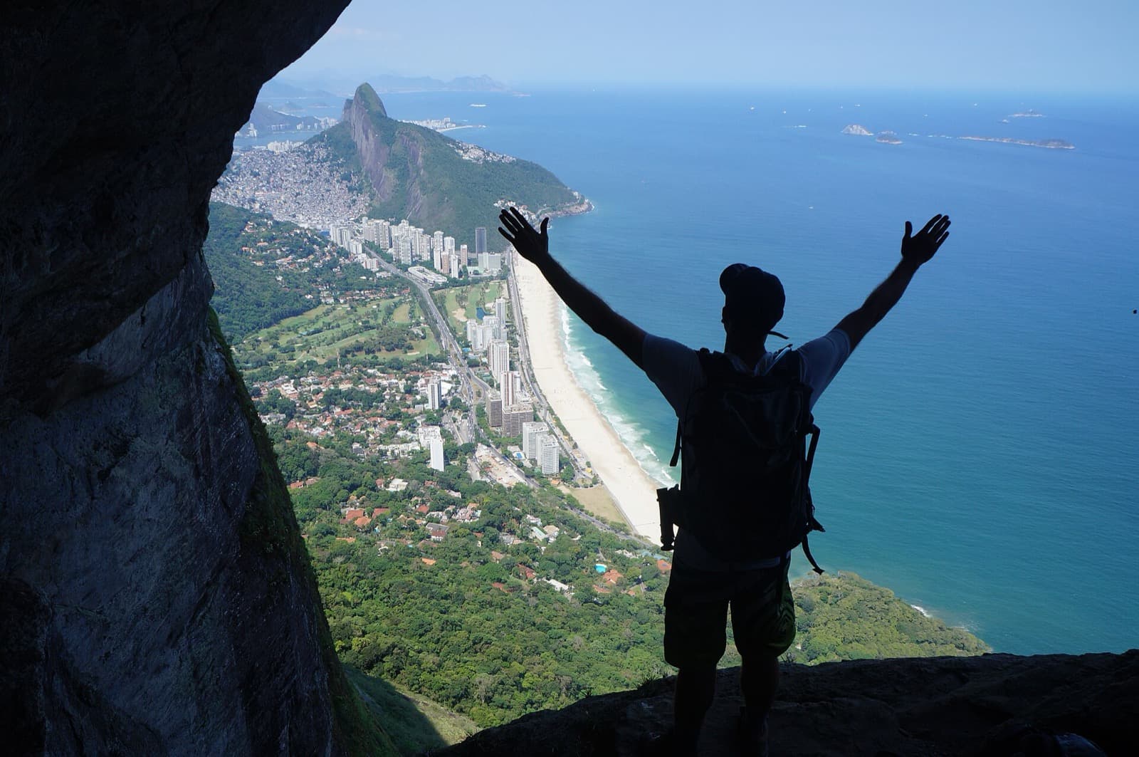 Trilheiro de braços abertos na Garganta do Céu, com São Conrado e o Morro Dois Irmãos ao fundo