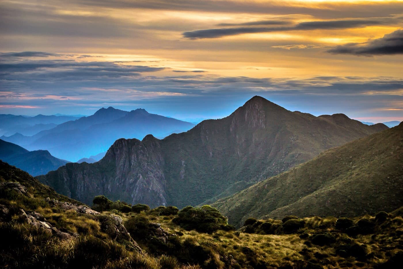 Pico do Capim Amarelo ao entardecer, visto da trilha da Travessia da Serra Fina, com serras azuladas ao fundo