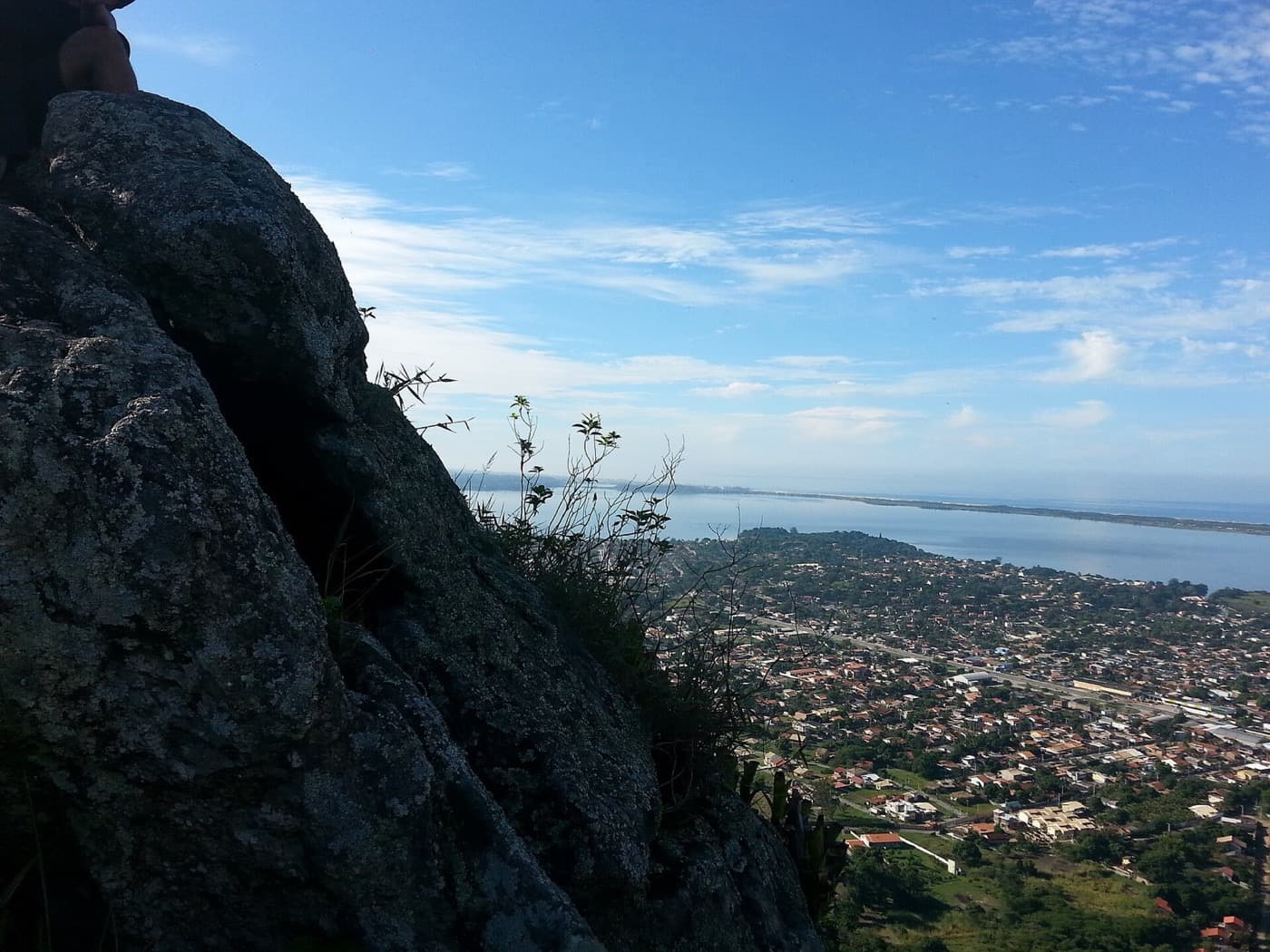 Vista do alto da Pedra do Macaco para os bairros de Maricá e a lagoa, ao lado de uma parede de rocha