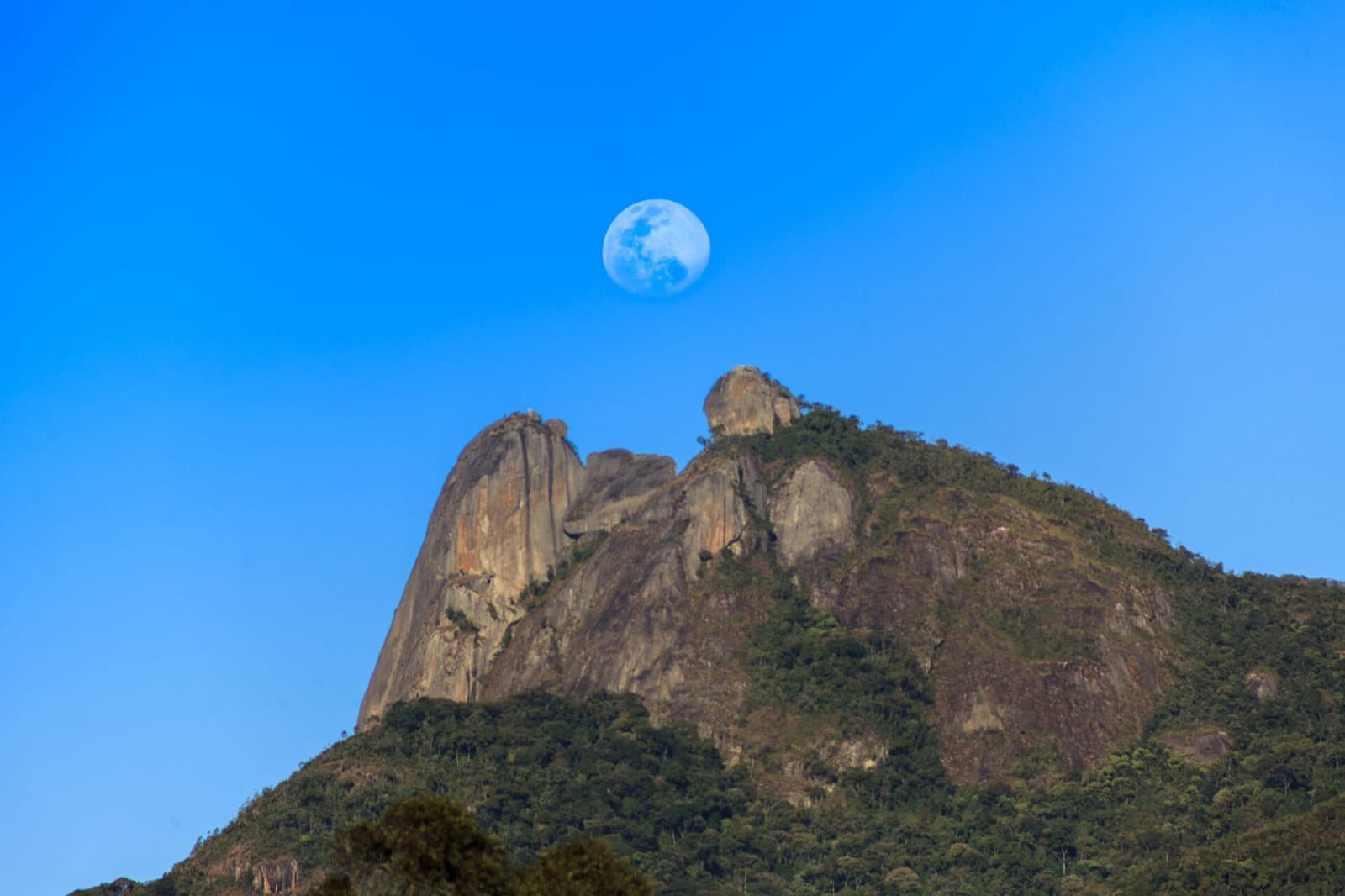 Lua cheia nascendo acima do perfil rochoso da Pedra Selada em céu azul