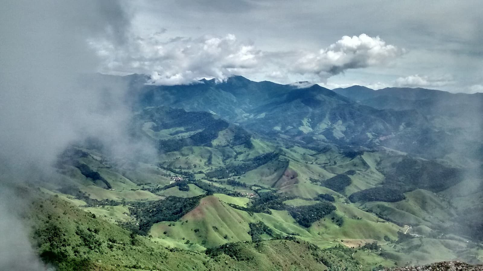 Vista do alto da Pedra Selada sobre os morros e pastos da Mantiqueira, com nuvens no horizonte