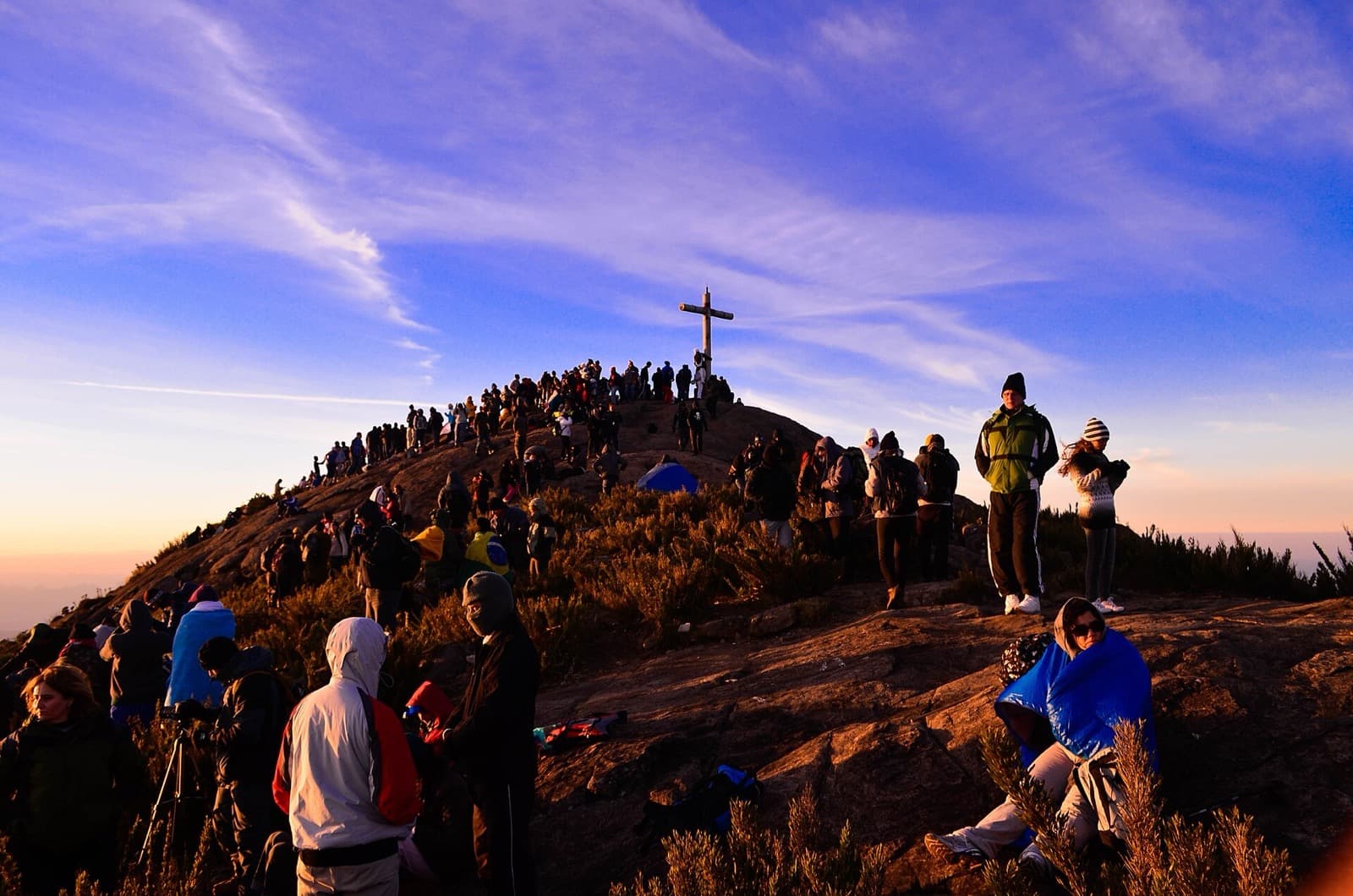 Montanhistas agasalhados em volta do cruzeiro no cume do Pico da Bandeira ao amanhecer