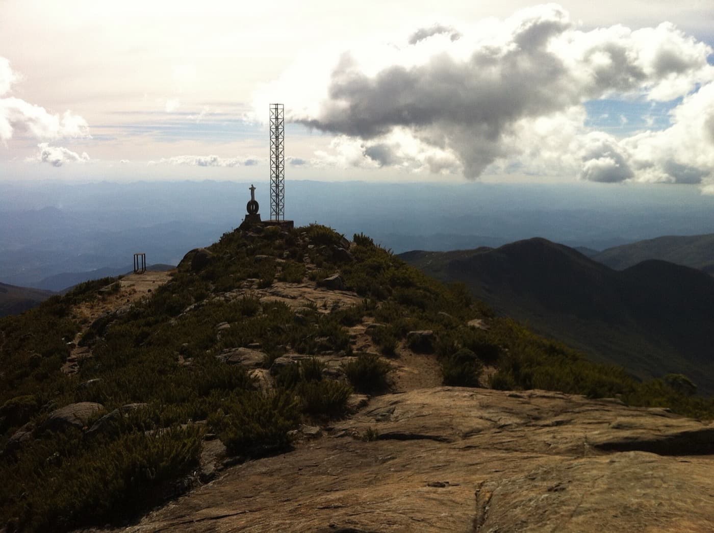 Último trecho de lajes e arbustos até o cume do Pico da Bandeira, com a torre metálica e uma imagem de Cristo no topo