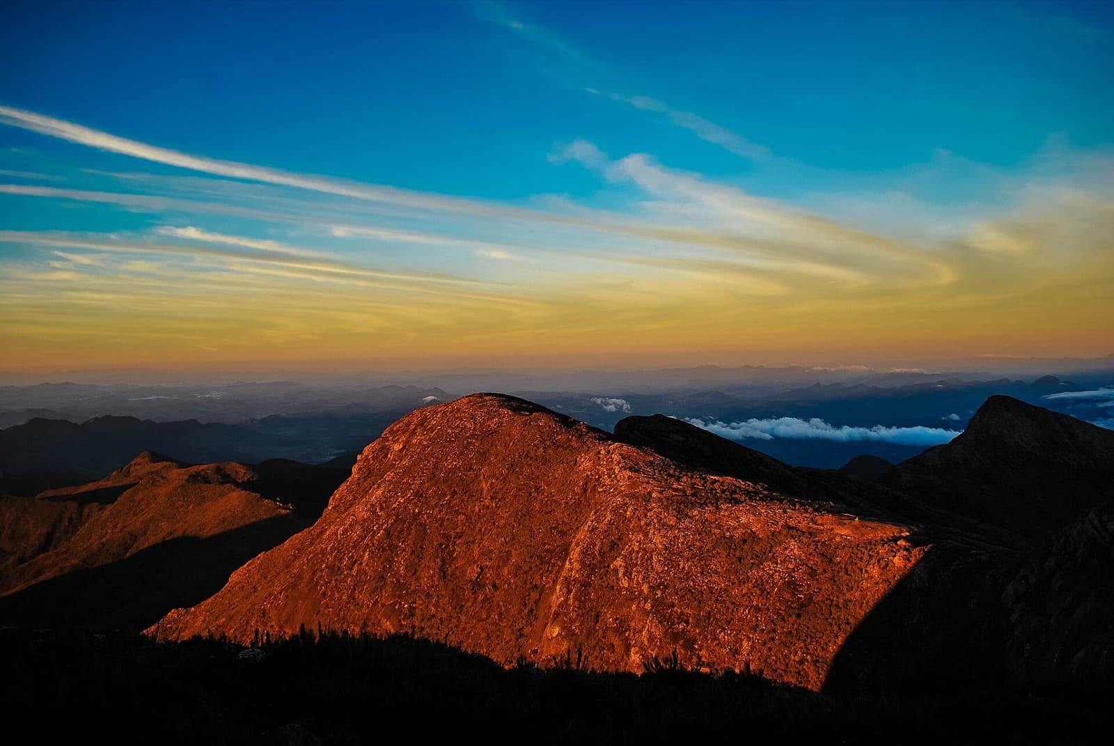 Pico do Cristal iluminado em tons de laranja pelo nascer do sol, visto do alto do Pico da Bandeira