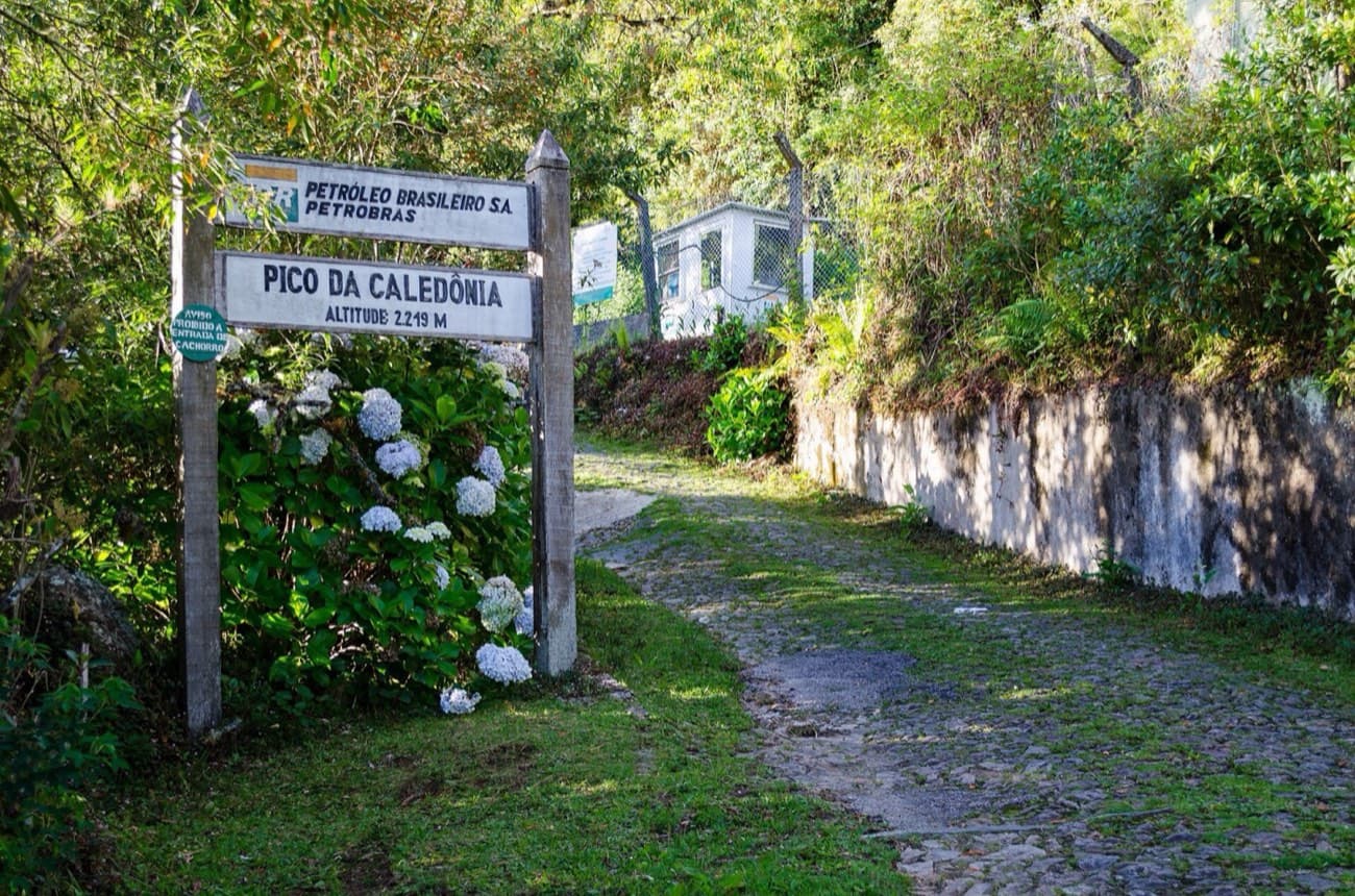 Portaria do Pico da Caledônia com placa da Petrobras e calçamento de pedra entre hortênsias