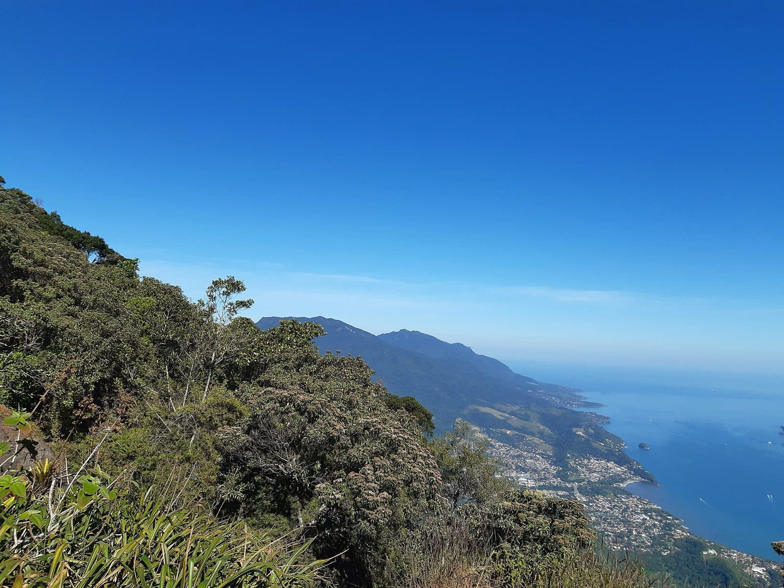 Encosta de mata da trilha do Baepi com a costa de Ilhabela e o mar ao fundo, sob céu azul