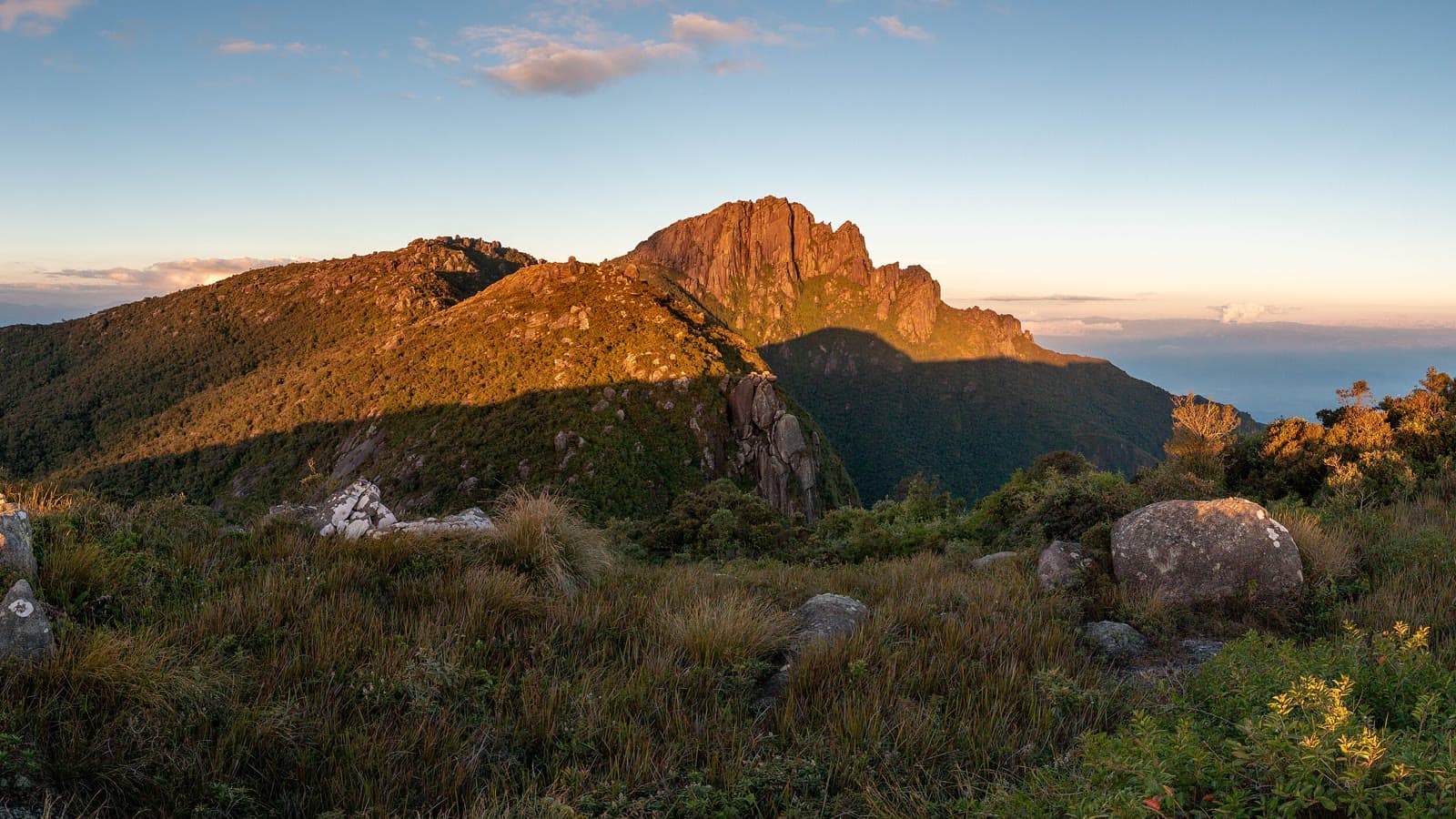 Paredões do Pico do Itaguaré iluminados pelo sol do fim de tarde, vistos dos campos de altitude onde ficam as áreas de acampamento