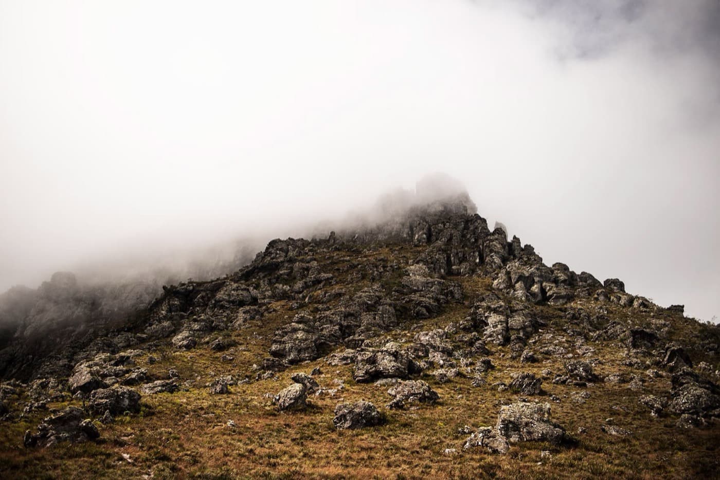 Encosta rochosa do cume do Pico do Itambé sendo encoberta pela neblina