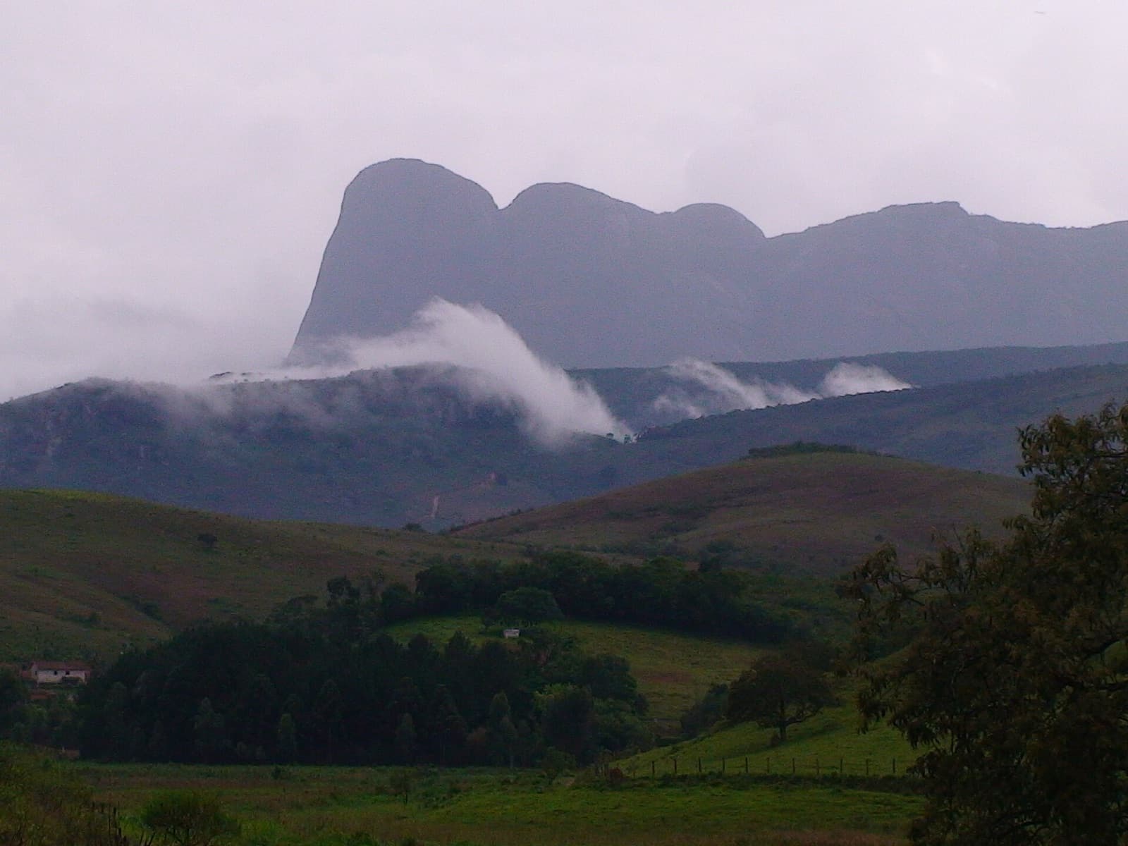Pico do Papagaio parcialmente coberto pela névoa de inverno, acima de morros e matas