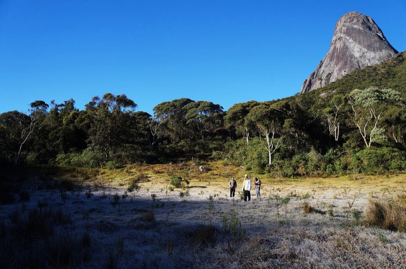 Campo coberto de geada no Vale dos Deuses ao amanhecer, com caminhantes e uma torre de granito ao fundo