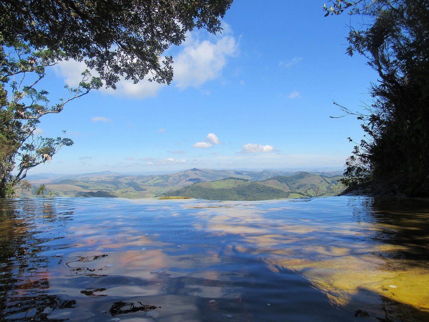 Superfície lisa do córrego no alto da Janela do Céu refletindo o céu, com montanhas no horizonte