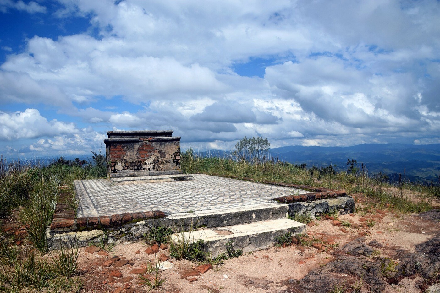 Ruínas da capela no alto do Pico do Pião: piso de ladrilhos e o altar de tijolos sob céu com nuvens