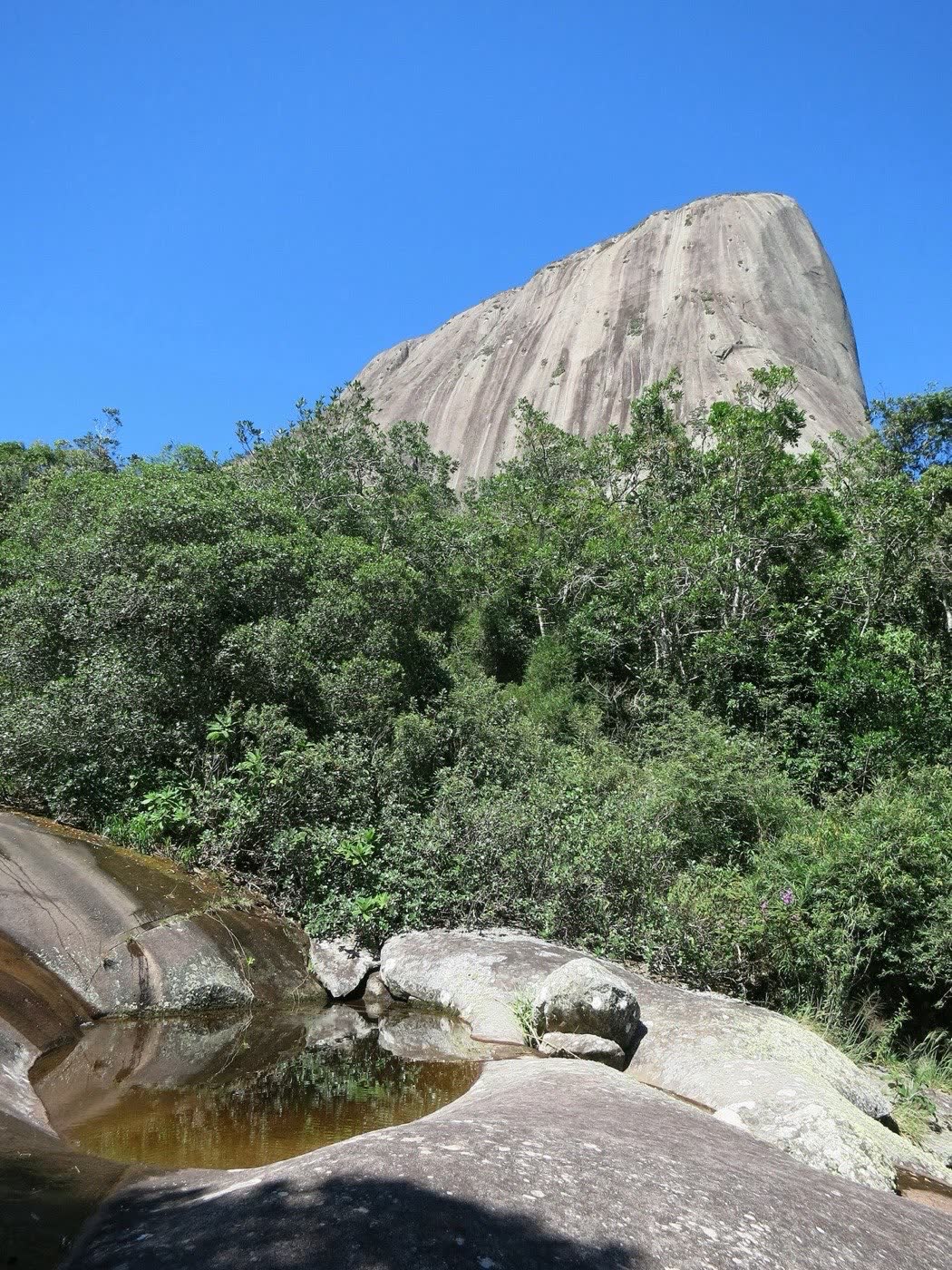Piscina natural escavada na rocha, com a Pedra Azul ao fundo e mata ao redor