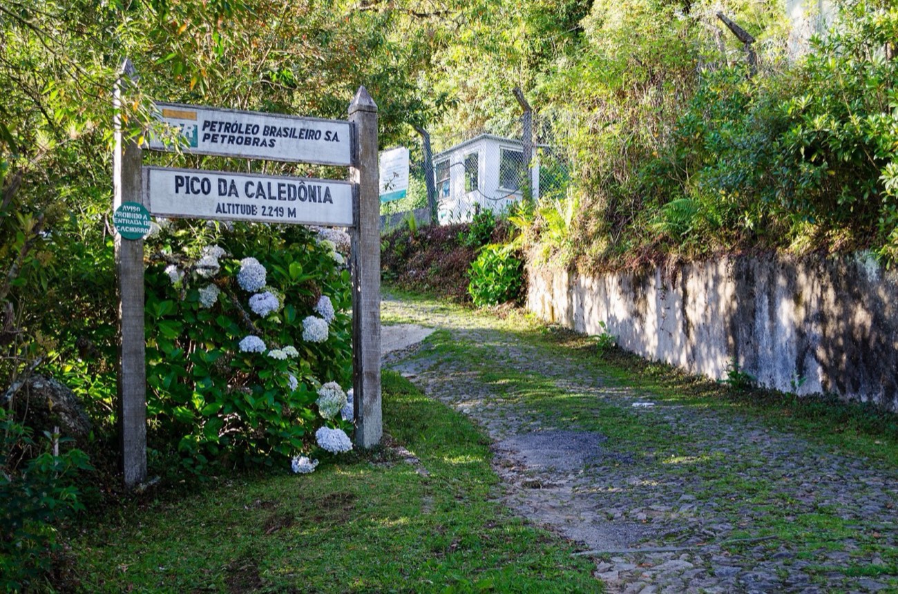 Placa e portaria do Pico da Caledônia, com calçamento de pedra e hortênsias