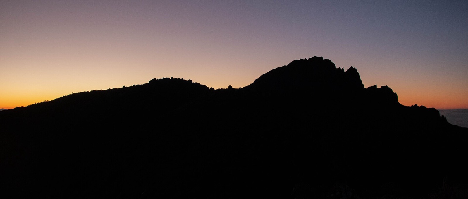 Silhueta do Pico do Itaguaré ao amanhecer, com o céu laranja atrás da crista rochosa